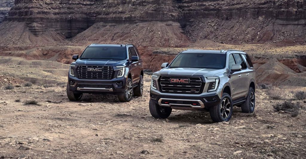 2025 GMC Yukon XL SUVs parked in a rugged desert canyon setting, showcasing their bold front grille, off-road capability, and premium exterior design against scenic rock formations.