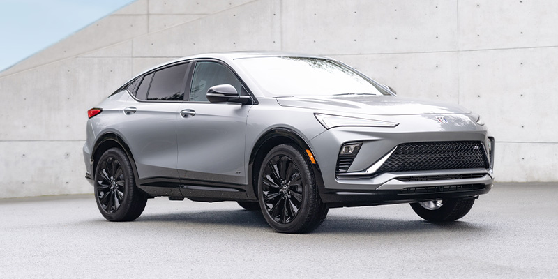 2025 Buick Envista in silver parked near a modern concrete building, highlighting its sleek crossover design and contemporary styling.