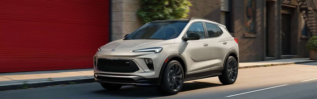 A Buick Encore GX ST driving on a city street with a red garage door in the background.