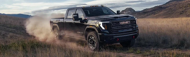 Black GMC Sierra HD AT4 raising a trail of dust while crossing a dry grass field below rolling hills