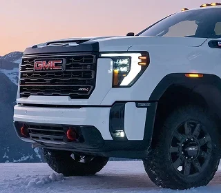 Front end of a white GMC Sierra HD AT4 pickup in snow at dusk