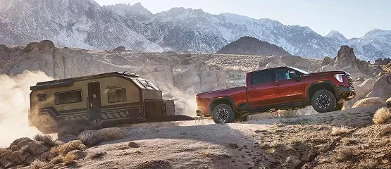Red GMC Sierra HD pickup towing a travel trailer on a mountain trail