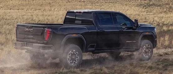 Black GMC Sierra HD AT4 pickup driving through a dry grass field