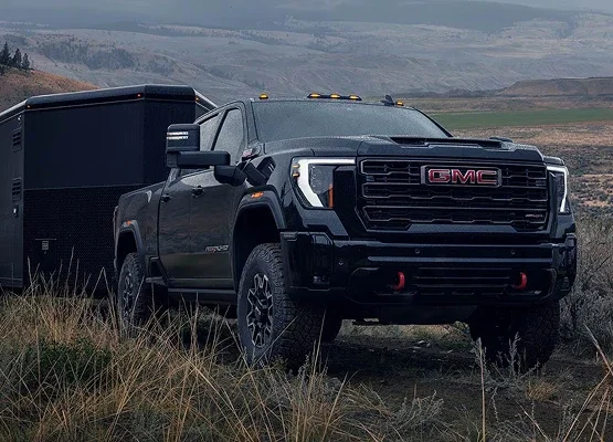 Black GMC Sierra HD AT4 pickup hitched to an enclosed trailer in open country