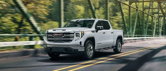 2026 GMC Sierra 1500 crew cab in white crossing a steel truss bridge, front three-quarter view