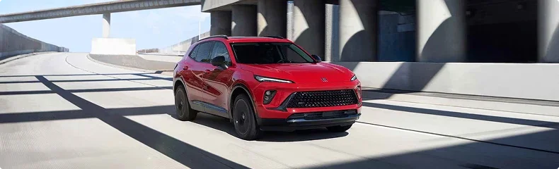 Red Buick Envision driving through a sunlit concrete highway interchange