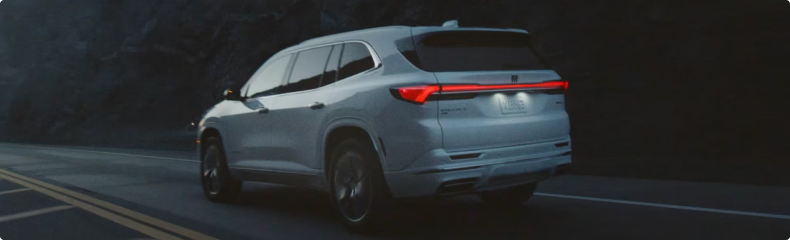 Rear three-quarter view of a white Buick Enclave driving on a dark mountain road