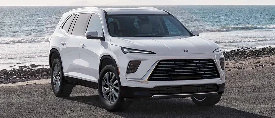 2026 Buick Enclave in white parked on a rocky shoreline with the ocean behind it, front three-quarter view