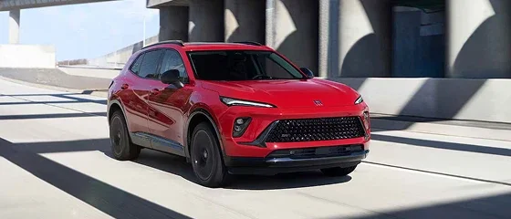 2026 Buick Envision in red driving beneath a concrete overpass, front three-quarter view
