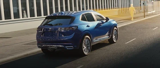 2026 Buick Envision in blue driving along a city street past a pedestrian crossing, rear three-quarter view