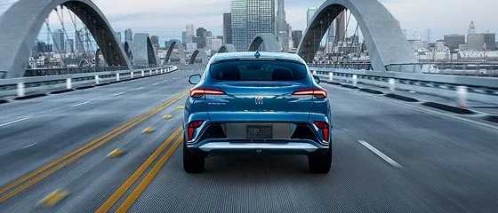 2026 Buick Envista Preferred in blue driving across a bridge toward a city skyline, rear view