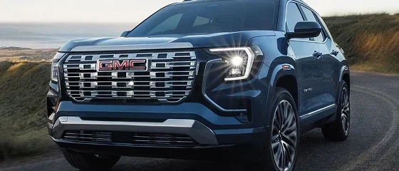 2027 GMC Terrain Elevation in dark blue on a coastal road with its headlamps lit, front three-quarter view