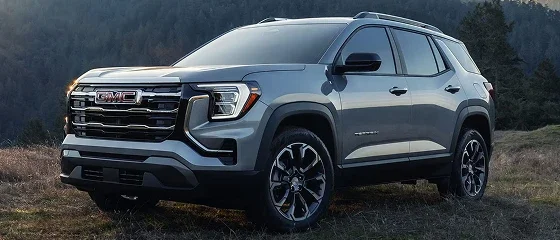 2027 GMC Terrain Elevation in gray parked on a grassy hillside with pine trees behind it, front three-quarter view