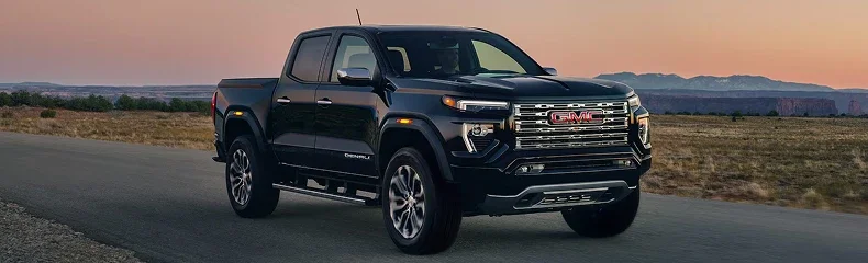 Black GMC Canyon Denali pickup on an open road at sunset