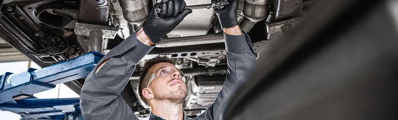 Service technician in safety glasses working beneath a raised vehicle on a lift