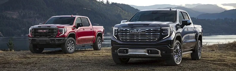 Red and black GMC Sierra pickups parked on a bluff above a lake