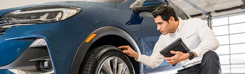 Service adviser with a tablet inspecting the front wheel of a blue Buick SUV