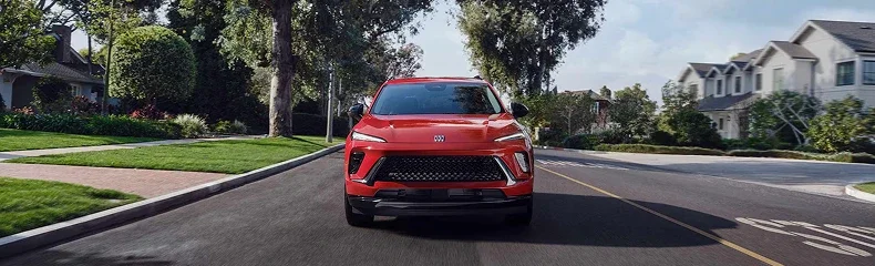 Front view of a red Buick crossover driving toward the camera on a residential street
