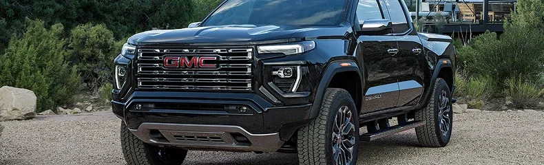 Black GMC Canyon Denali parked on a gravel lot beside desert shrubs