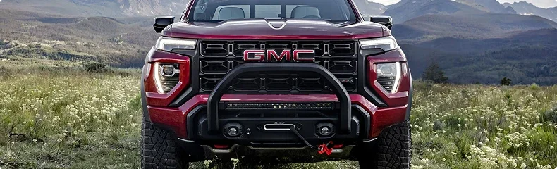 Red GMC Canyon AT4X with a front bull bar and winch parked in a mountain meadow